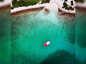 Aerial view of a boat navigating through crystal-clear turquoise waters, showcasing the beauty of a secluded beach and vibrant marine environment.