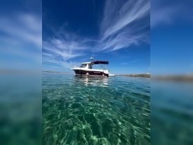 Two individuals enjoy a refreshing swim in crystal-clear waters with a boat anchored nearby, capturing the essence of a perfect day on the water.