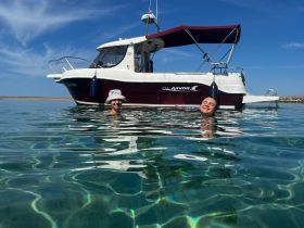 Two friends enjoy a refreshing swim in crystal-clear waters beside their boat, capturing the essence of summer fun and adventure on the water.