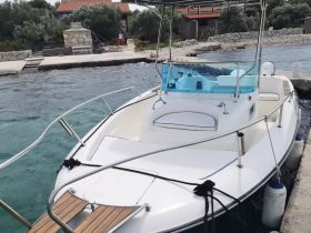 A sleek boat docked at a picturesque waterfront, surrounded by lush greenery and a charming stone structure, perfect for a day on the water.