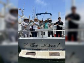 A joyful group celebrates their successful fishing trip aboard 'The Fresh One' in Ensenada, showcasing their impressive catch against a sunny backdrop.