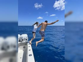 A couple joyfully jumps off the side of a boat into the vibrant blue waters, capturing the thrill of summer adventures on the water.