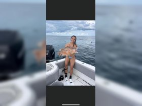 A joyful angler proudly displays her catch aboard a boat, showcasing the thrill of fishing on the open water.