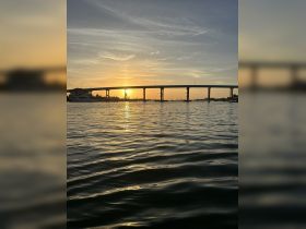 A stunning sunset view over the water, framed by a bridge, creating a picturesque scene perfect for evening boat rides.