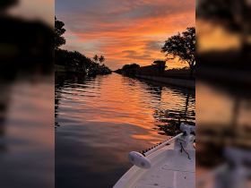 A serene sunset view from the bow of a boat, reflecting vibrant colors on the calm water, perfect for evening cruises or peaceful moments on the water.