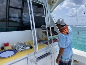 A crew member prepares food on the grill aboard a boat, showcasing the onboard catering amenities for a delightful dining experience on the water.