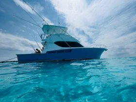 A fishing boat navigates through crystal-clear waters, with a person preparing fishing gear on board — an ideal scene for fishing enthusiasts and ocean adventures.
