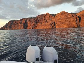 A stunning view of rugged cliffs illuminated by the sunset, captured from a boat on tranquil waters — perfect for scenic boat tours and nature lovers.