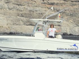 A man gives a thumbs up while standing on a fishing charter boat named 'Fish 'N Chips,' showcasing a perfect day on the water.