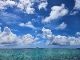A stunning view of a serene coastline with an island in the distance, framed by vibrant blue skies and fluffy clouds — perfect for showcasing the beauty of tropical destinations.
