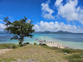 A vibrant scene of visitors enjoying a beautiful beach day, with boats anchored nearby and stunning turquoise waters — perfect for island hopping adventures.