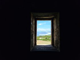 A view through a stone window showcasing a scenic landscape with ocean and greenery, but the focus is unclear.