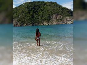 A woman stands in the shallow waters of a picturesque beach, gazing at the lush island backdrop — a perfect scene for tropical getaways and relaxation.