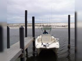 A speedboat is docked at a pier with a fisherman at the helm, ready for a day of fishing on the water.