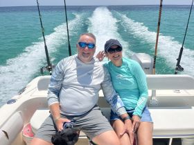 A happy couple enjoys a fishing trip on a boat, capturing the joy of their time on the water with smiles and beautiful turquoise waves in the background.