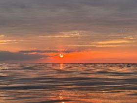 A stunning sunset reflects on calm waters, creating a picturesque scene perfect for evening boat cruises.