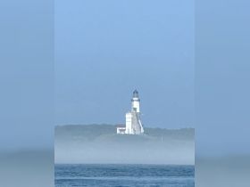 A distant view of a lighthouse shrouded in mist, creating an atmospheric scene on the water.