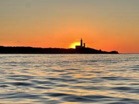 A stunning sunset view behind a lighthouse, casting a warm glow over the tranquil waters — a perfect moment for coastal exploration and photography.