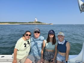 A cheerful group poses for a photo on a boat with a scenic lighthouse in the background, capturing the joy of a perfect day on the water.