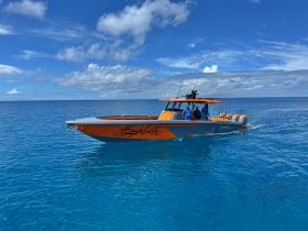 A vibrant boat named 'Boom Bastic' cruises through crystal-clear waters, showcasing an exciting day on the ocean with friends.