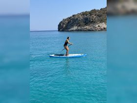 A woman paddleboards in crystal-clear waters, showcasing the beauty of outdoor water activities against a stunning island backdrop.