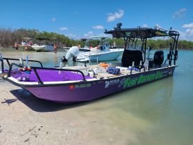 A vibrant flat-bottom boat is anchored in shallow waters, with a group of people enjoying a fishing trip in a picturesque setting.