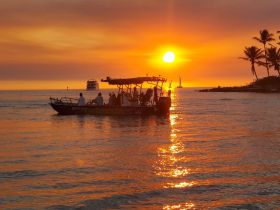 A group enjoys a scenic sunset cruise on the water, with vibrant colors reflecting off the ocean — an ideal moment for relaxation and adventure.