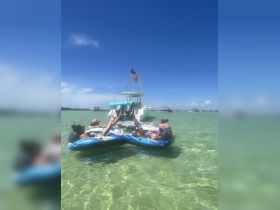 A lively group enjoys a fun day on the water, relaxing on inflatable tubes while anchored near a boat — perfect for summer adventures and sandbar stops.