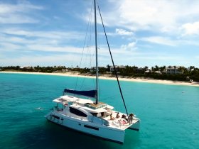 An aerial view of a catamaran anchored in stunning turquoise waters, with guests enjoying the sun and swimming nearby — a perfect scene for a tropical getaway.