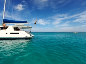 A thrilling moment captured as a person jumps off a catamaran into the crystal-clear waters, showcasing the excitement of water activities during a sunny day on the boat.