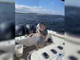A young boy proudly holds up his catch while fishing on a boat, showcasing a fun and memorable day on the water.
