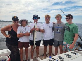 A group of friends proudly displays their catch, a shark, while enjoying a fishing trip on the water — a perfect memory of adventure and camaraderie.