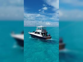 A fishing boat named 'Cape Escapade' navigates through crystal-clear waters, with a group of people onboard enjoying their day at sea.
