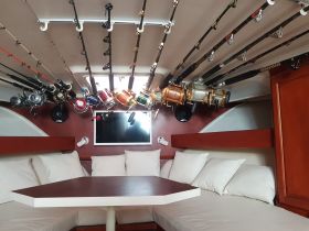 Interior view of a boat cabin featuring a cozy seating area and an array of fishing rods and reels, perfect for fishing enthusiasts looking to enjoy their time on the water.