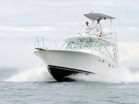 A sleek speedboat cuts through the water, showcasing its design and performance with two individuals at the helm, ideal for thrilling adventures on the open sea.