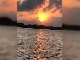 A stunning sunset casts a warm glow over the water, creating a picturesque reflection — perfect for capturing the beauty of nature during a boating trip.