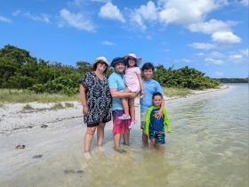 A joyful family poses together on the beach, enjoying a sunny day by the water — perfect for creating lasting memories during family vacations.