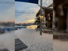 A picturesque sunset view from the beach, with guests enjoying the water and a lively atmosphere near the dock — perfect for a relaxing evening by the shore.
