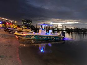 A vibrant speedboat named 'Team Vinson Charters' docked at a beachside location, illuminated by colorful lights against a twilight sky — perfect for evening charters and adventures.