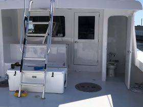 A clean and spacious interior view of a boat's helm area, featuring a YETI cooler and access to a bathroom, ideal for comfort during outings.