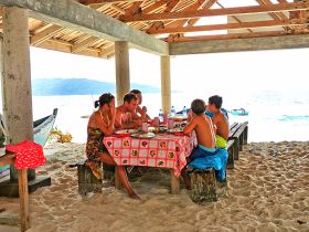 A group of friends and family enjoy a meal together at a beachside dining area, creating memorable moments in a picturesque setting.