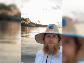 A man takes a selfie by the water during sunset, capturing the serene reflections and tranquil atmosphere — perfect for memorable moments on the water.
