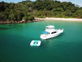 Aerial view of a sleek yacht anchored in crystal-clear turquoise waters, surrounded by lush greenery — perfect for serene getaways or island explorations.