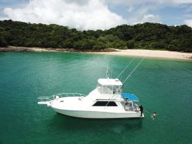 A group enjoys a tropical getaway with a boat anchored near a sandy beach, featuring a child swimming nearby — perfect for family adventures in paradise.