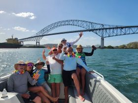 A lively group of friends celebrates aboard a boat with a stunning bridge in the background, capturing the joy of their day on the water.