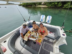 A cheerful group enjoys a delicious meal aboard a boat, showcasing a perfect blend of fishing and dining experiences in a serene setting.