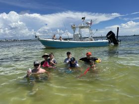 A lively group enjoys a fun day swimming in shallow waters with a boat anchored nearby, perfect for family outings and water adventures.