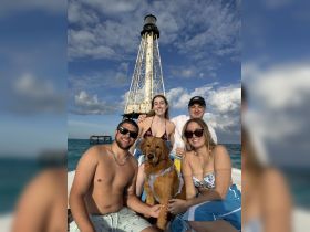 A cheerful group poses with a golden retriever on a boat near a lighthouse, capturing a fun moment on the water — perfect for memorable outings with friends and pets.