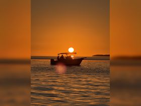 A serene sunset silhouette of a boat on the water, capturing a tranquil moment perfect for evening cruises.