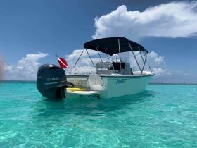 A sleek speedboat anchored in crystal-clear turquoise waters, showcasing its elegant design against a backdrop of fluffy clouds.